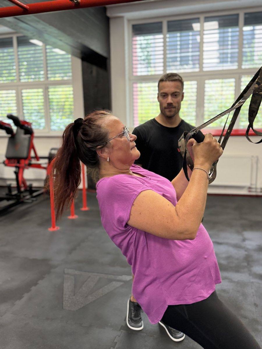 Klientka 40+ cvičí na TRX s dopomocí trenéra
